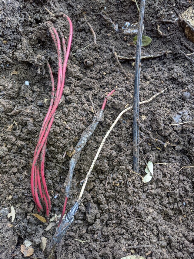 Multiple wires in the ground alongside a fiber optic cable run, two wires have tape wrapped around part
