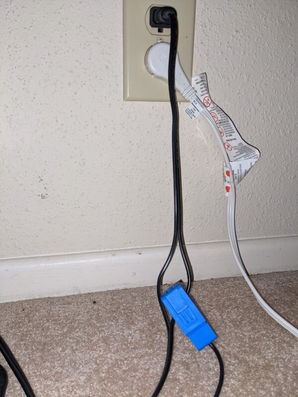 A blue current transformer around one leg of a lamp cord cable.  The cable is plugged into the wall.